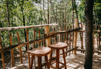 Barra y taburetes de madera en la terraza del Tree House de Cosy Cabins, rodeado de bosque en Limburg, Bélgica.