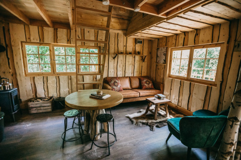 Acogedora sala de casa en el árbol con paredes de madera, sofá y grandes ventanas en el bosque de Limburgo.