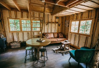 Acogedora sala de casa en el árbol con paredes de madera, sofá y grandes ventanas en el bosque de Limburgo.