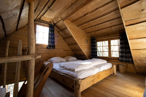 Dormitorio de casa de árbol de madera con cama doble en Cosy Cabins, bosque de Limburg, Bélgica.