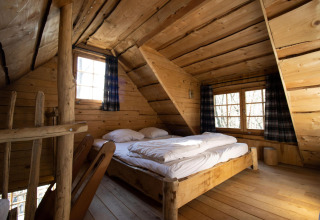 Dormitorio de casa de árbol de madera con cama doble en Cosy Cabins, bosque de Limburg, Bélgica.