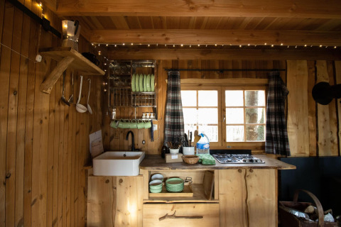 Pequeña cocina de madera con ventana, fogón y utensilios en Tree House Cosy Cabins en el bosque de Limburg.