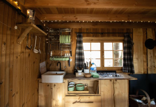 Pequeña cocina de madera con ventana, fogón y utensilios en Tree House Cosy Cabins en el bosque de Limburg.