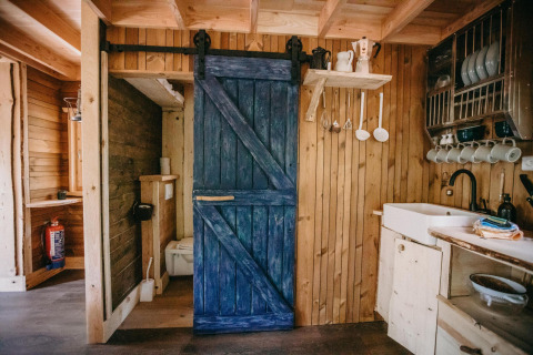 Interior de una pequeña casa en el árbol en el bosque de Limburg, Bélgica, con paredes de madera y puerta azul.