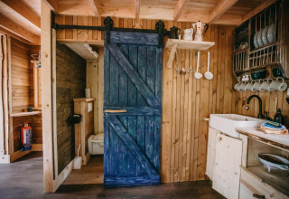 Interior de una pequeña casa en el árbol en el bosque de Limburg, Bélgica, con paredes de madera y puerta azul.