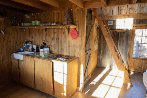 Interior de casa de árbol con paredes de madera, pequeña cocina y escalera en el bosque de Limburg, Bélgica.