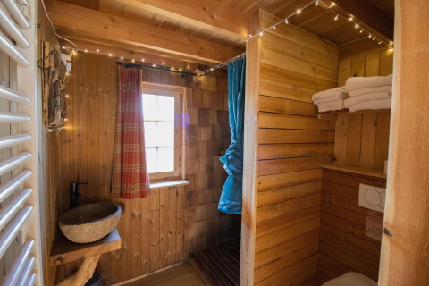 Baño de madera con lavabo de piedra, toallas y ventana en Tree House 1, Cosy Cabins, bosque de Limburg, Bélgica.