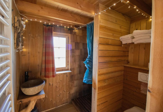 Baño de madera con lavabo de piedra, toallas y ventana en Tree House 1, Cosy Cabins, bosque de Limburg, Bélgica.