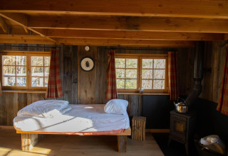 Tree House 1 en Cosy Cabins, bosque de Limburg, Bélgica. Dormitorio rústico con cama y estufa de leña.