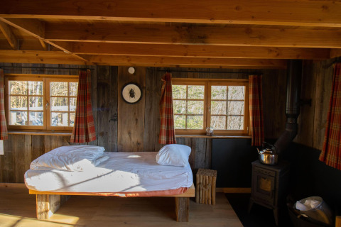 Tree House 1 a Cosy Cabins nella foresta di Limburg, Belgio. Stanza rustica con letto e stufa a legna.
