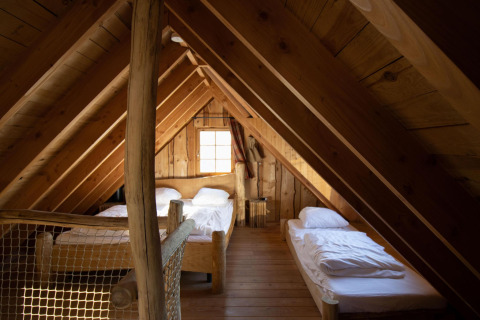 Ático acogedor con paredes de madera y tres camas individuales en Tree House 1 de Cosy Cabins, Limburg, Bélgica.