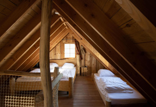 Ático acogedor con paredes de madera y tres camas individuales en Tree House 1 de Cosy Cabins, Limburg, Bélgica.