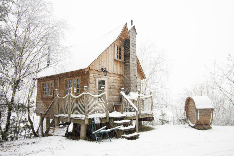 Casa del árbol cubierta de nieve en Cosy Cabins, bosque de Limburg, Bélgica, escena invernal tranquila.