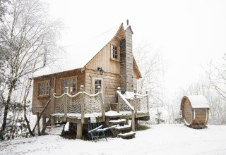 Casa del árbol cubierta de nieve en Cosy Cabins, bosque de Limburg, Bélgica, escena invernal tranquila.
