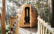 Een gezellige houten boomhut met een rond dak, genesteld tussen hoge dennenbomen in een bos in Limburg, België.