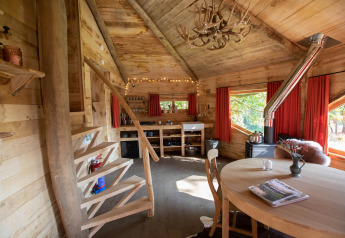 Accogliente casa sull'albero in legno nel Limburgo, in Belgio, con arredamento rustico, tavolo da pranzo rotondo e scale a chiocciola.