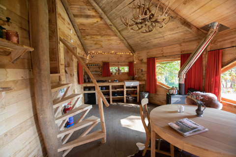 Accogliente casa sull'albero in legno nel Limburgo, in Belgio, con arredamento rustico, tavolo da pranzo rotondo e scale a chiocciola.