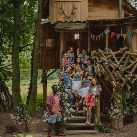 Grupo de jóvenes adultos con atuendos de temática campestre posando en las escaleras de una casa del árbol decorada en Limburgo, Bélgica.