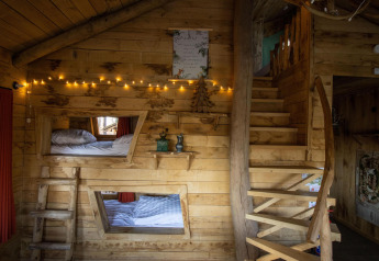 Gezellig houten boomhut interieur met feeërieke lichtjes, stapelbedden, rustieke trap en natuurlijke houtaccenten in België.