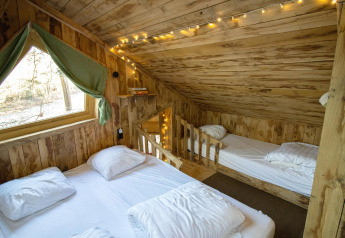 Gezellige houten boomhut slaapkamer met koordverlichting, twee bedden en een raam met groene gordijnen in België.