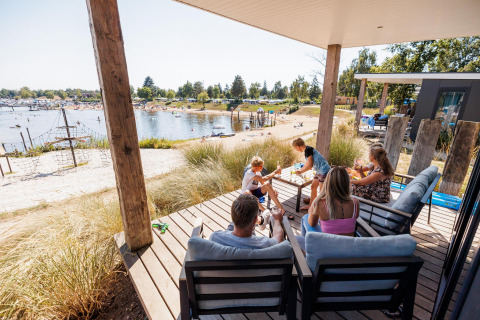 Famille se détendant sur la terrasse du Beach lodge | Port à Vakantiepark Leukermeer, Pays-Bas.