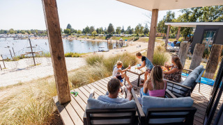 Familia disfrutando en la terraza del Beach lodge | Port en Vakantiepark Leukermeer, Países Bajos.