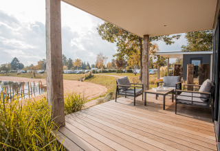 Terraza de madera con sillones y vista al lago en Beach lodge Port, Vakantiepark Leukermeer, Países Bajos.