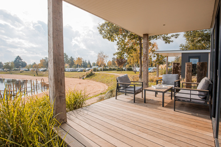 Terraza de madera con sillones y vista al lago en Beach lodge Port, Vakantiepark Leukermeer, Países Bajos.