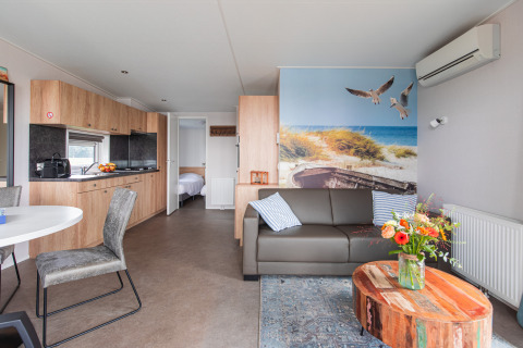 Moderne Lodge mit Holzmöbeln, gemütlichem Sofa, großem Strandbild und offener Küche in Vakantiepark Leukermeer.