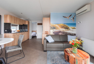 Modern lodge with wood decor, comfortable sofa, large beach mural, and open kitchen at Vakantiepark Leukermeer.