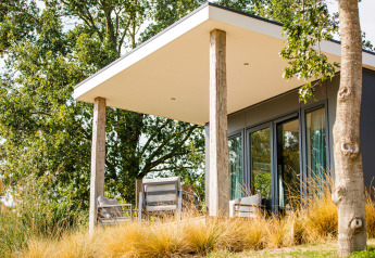 Moderne Lodge mit Terrasse und Gartenmöbeln im Vakantiepark Leukermeer, Niederlande, umgeben von Bäumen.