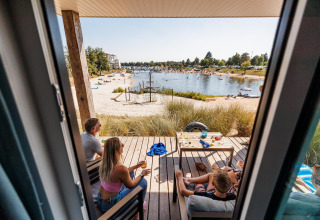 Blick aus einer Strandlodge im Vakantiepark Leukermeer, Niederlande, mit Menschen auf der Terrasse am See.