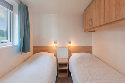 Dos camas individuales con ropa de cama blanca y armarios de madera en Beach lodge de Vakantiepark Leukermeer.