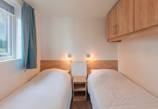 Dos camas individuales con ropa de cama blanca y armarios de madera en Beach lodge de Vakantiepark Leukermeer.