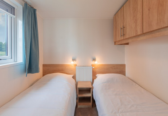 Deux lits simples avec draps blancs et armoires en bois, Beach lodge au Vakantiepark Leukermeer, Pays-Bas.