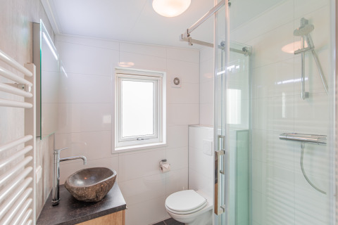 Moderne badeværelse med stenvask, bruser med glasdør og toilet på Beach lodge i Vakantiepark Leukermeer.