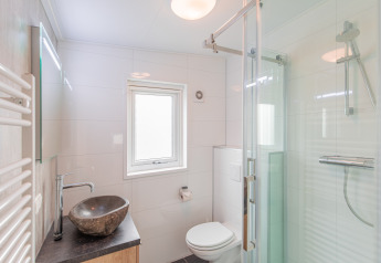 Baño moderno con lavabo de piedra, ducha de vidrio y WC en Beach lodge de Vakantiepark Leukermeer.