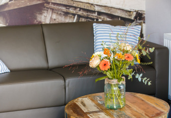 Gemütliches Wohnzimmer mit grauem Sofa, gestreiften Kissen und Blumenarrangement im Beach lodge in den Niederlanden.