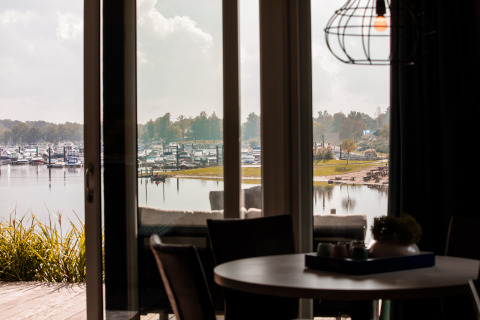 Vista desde una cabaña con grandes ventanas hacia un puerto deportivo con barcos en Vakantiepark Leukermeer.