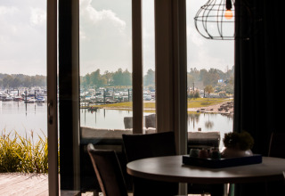 Vista desde una cabaña con grandes ventanas hacia un puerto deportivo con barcos en Vakantiepark Leukermeer.