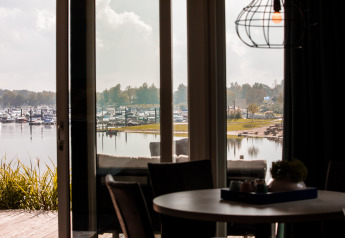 Vista desde una cabaña con grandes ventanas hacia un puerto deportivo con barcos en Vakantiepark Leukermeer.