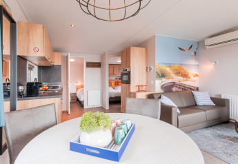 Lyst og moderne strandhytteinteriør med opholdsstue, køkken og strandtema-vægmaleri i Vakantiepark Leukermeer.