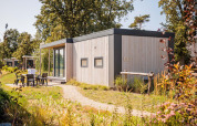 Casa pequeña Beach lodge en Vakantiepark Leukermeer, Países Bajos, rodeada de vegetación y área para sentarse.