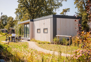 Casa pequeña Beach lodge en Vakantiepark Leukermeer, Países Bajos, rodeada de vegetación y área para sentarse.