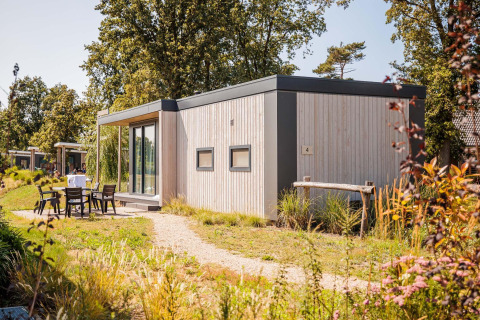 Moderne strandlodge op Vakantiepark Leukermeer in Nederland, tiny house met buitenzitje in het groen.