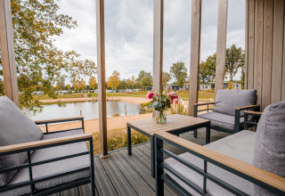 Vista desde la terraza del Beach Lodge en Vakantiepark Leukermeer, con muebles modernos y lago de fondo.