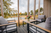 Vue depuis la terrasse du Beach Lodge à Vakantiepark Leukermeer avec des fauteuils modernes et un lac paisible.