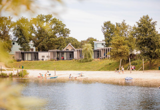 Zandstrand aan Leukermeer met Beach lodge tiny houses en gezinnen die ontspannen bij het water.