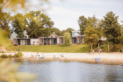 Beach at Vakantiepark Leukermeer with Island Beach lodge tiny houses and people enjoying the water and sand.
