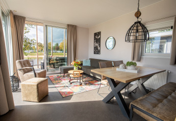 Moderne stue i en Beach Lodge ved Vakantiepark Leukermeer, Holland, med store vinduer og farverig indretning.